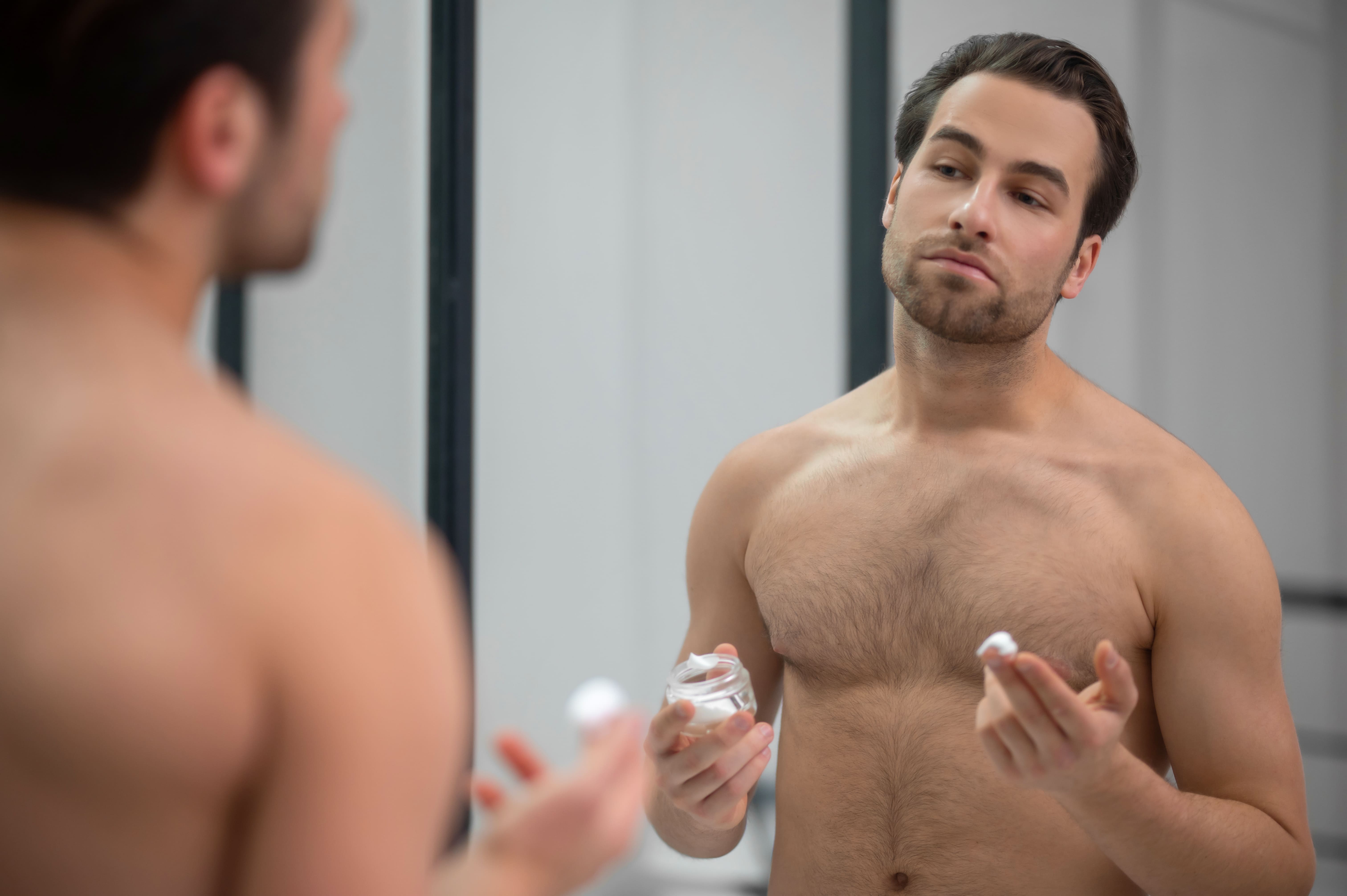 ragazzo allo specchio che mette la crema skincare uomo